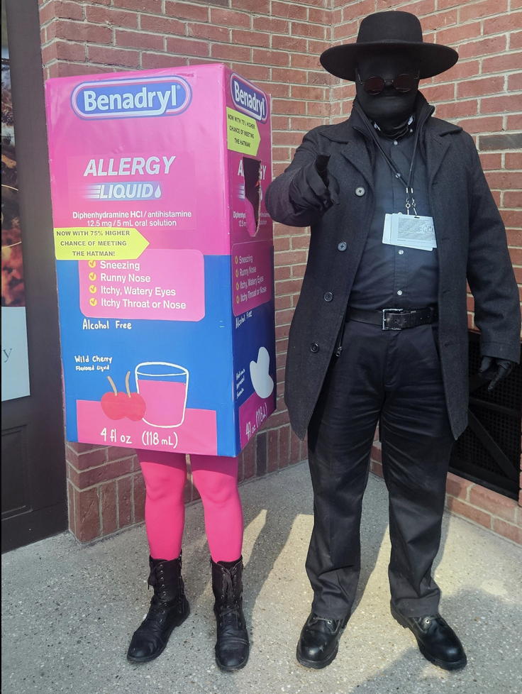A cosplayer dressed in black beside a giant Benadryl box, referencing a viral meme